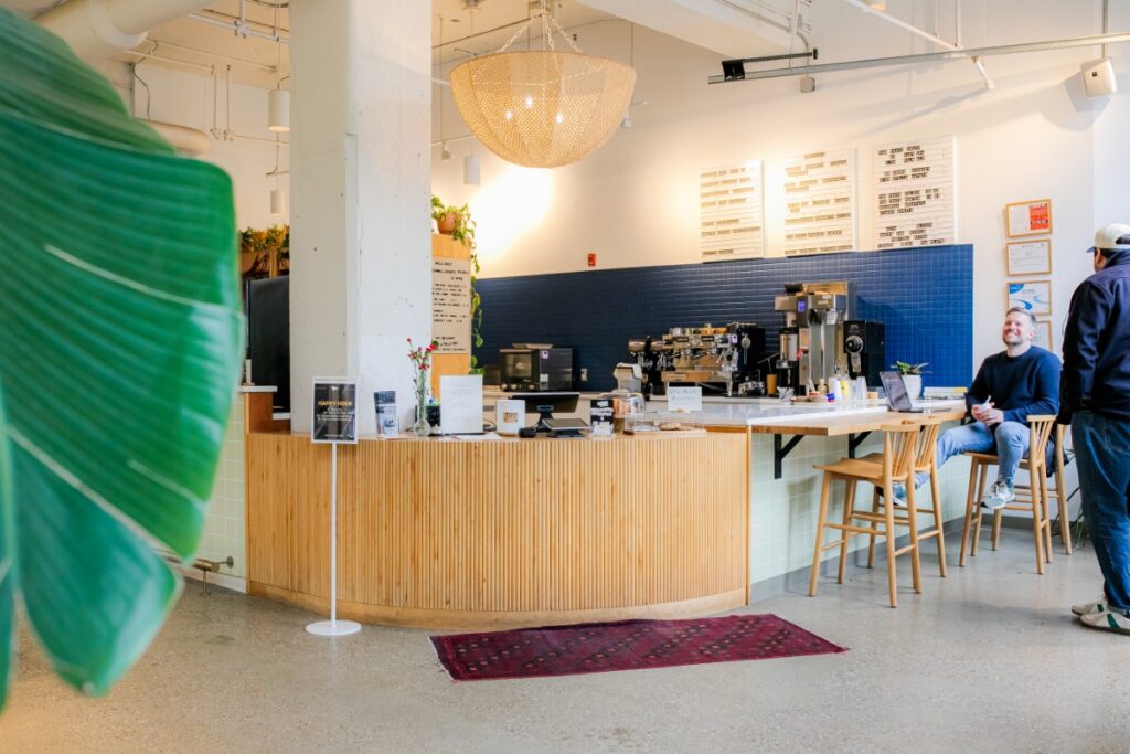 A sleek, sunlit cafe interior with a curved wooden service desk, blue tile accent wall, and remote workers sitting at Field Day in Lawrenceville.