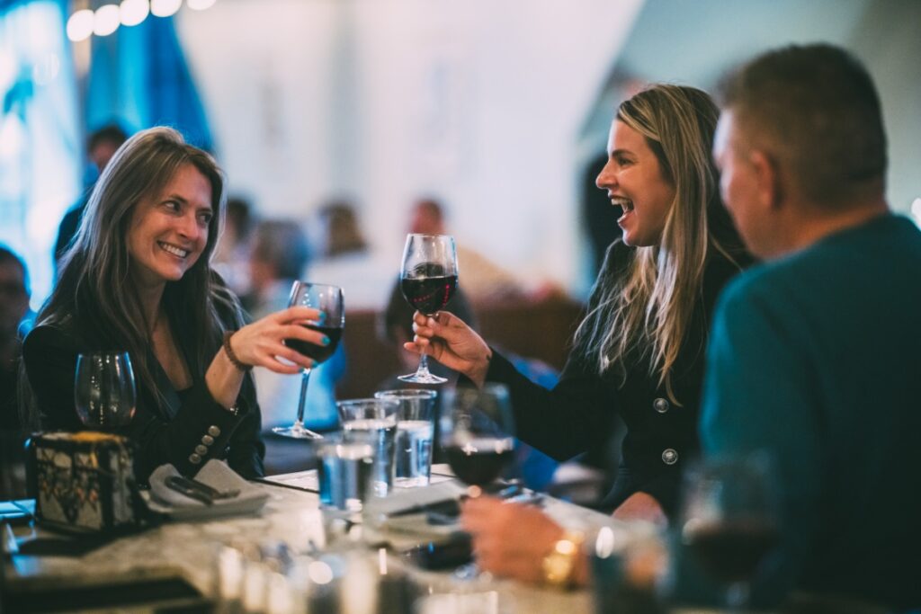 Friends laughing and drinking red wine at Vivo Kitchen restaurant in Sewickley.