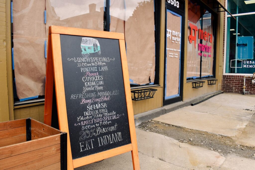 A sign with lunch specials sits in front of a papered window of Mera Market.