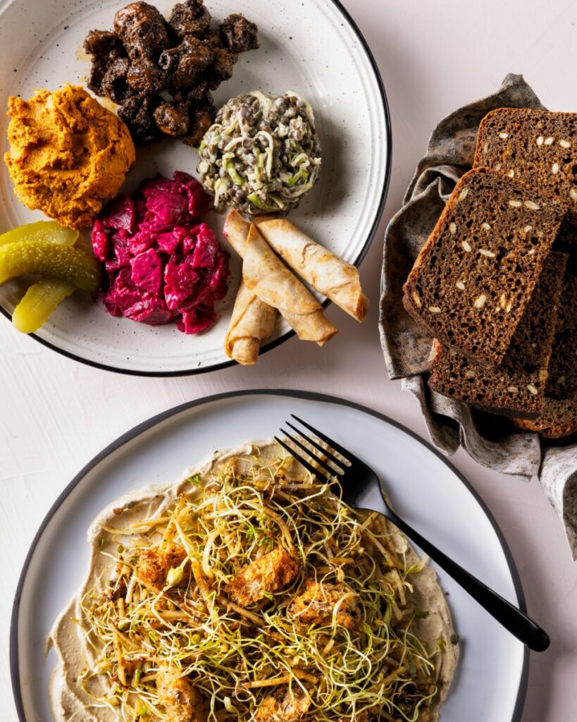 A spread of Central and Eastern European vegan dishes from Apteka in Pittsburgh, featuring dark seed rye bread, beet salad, pickles, and vegetable spreads.