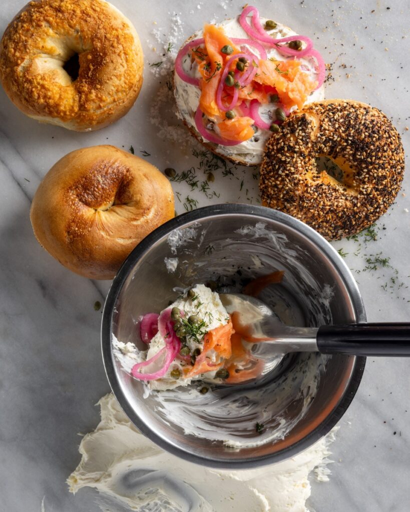 Assorted fresh bagels from Phat Bagel in Pittsburgh, featuring an everything bagel topped with cream cheese schmear, smoked salmon lox, pickled red onions, and capers.