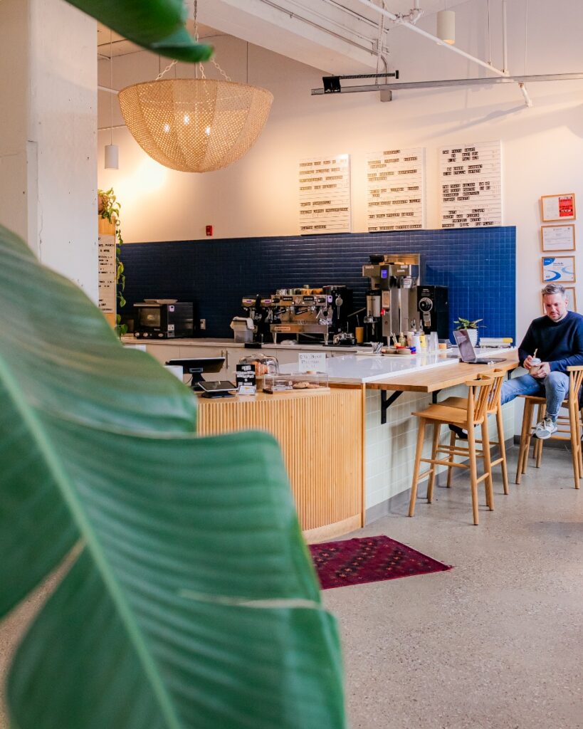 Inside the modern café and shared workspace at Field Day Coworking in Lawrenceville, Pittsburgh, featuring a blue tiled espresso bar and wooden bar stools.