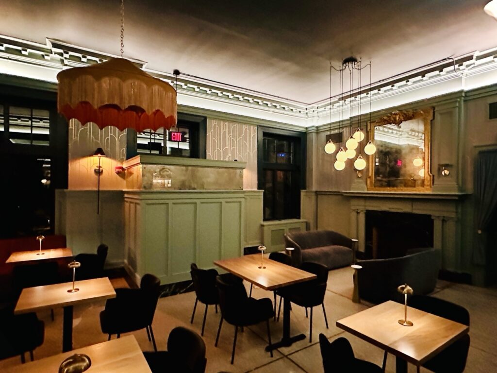 The dining room at Hey Babe with black chairs, wood tables and sage green wallpaper.