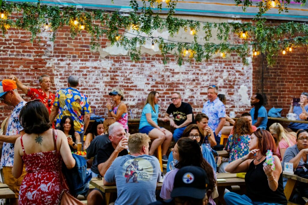 Crowd gathered at outdoor picnic tables in a brick patio beer garden under string lights at Golden Age Beer Co.