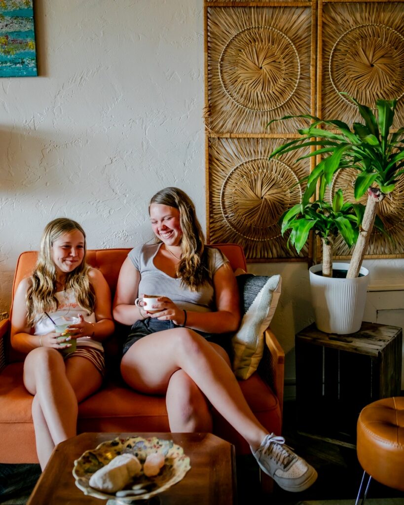 Two customers smiling and enjoying drinks on a couch inside Moonbeam Cafe.