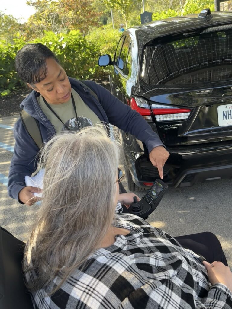 A woman shows another woman in a trackchair how to use the chair interface.