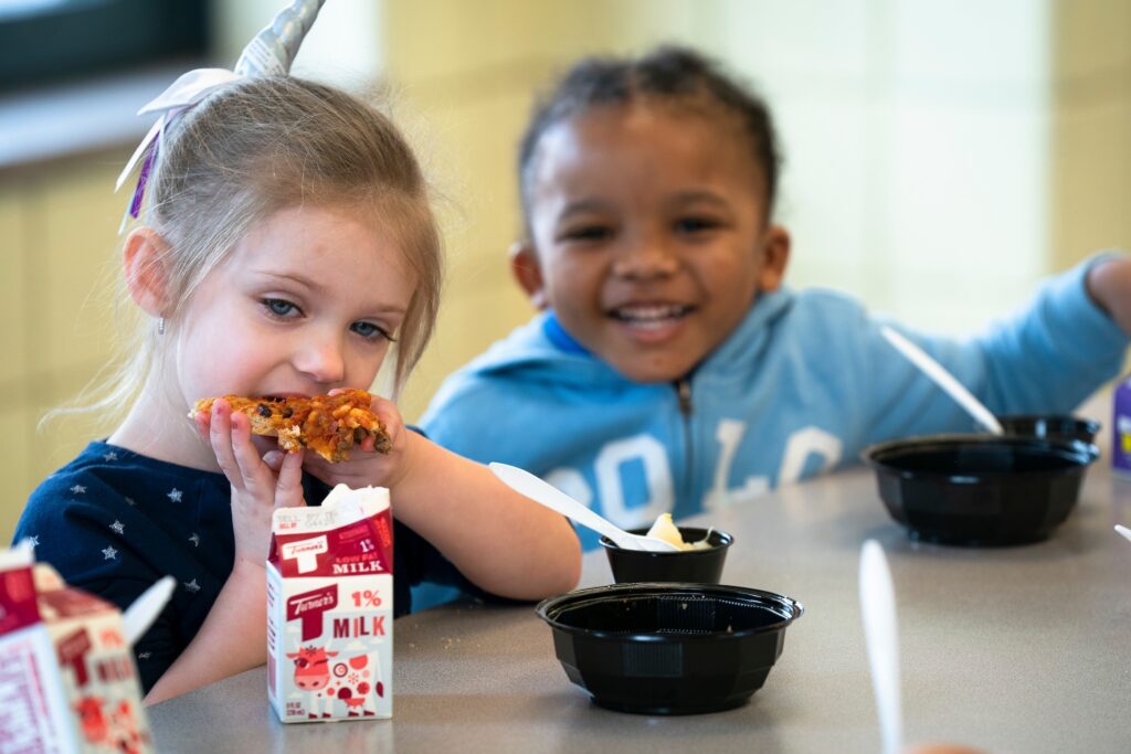 Two early elementary aged children eating lunch at a school lunch table.